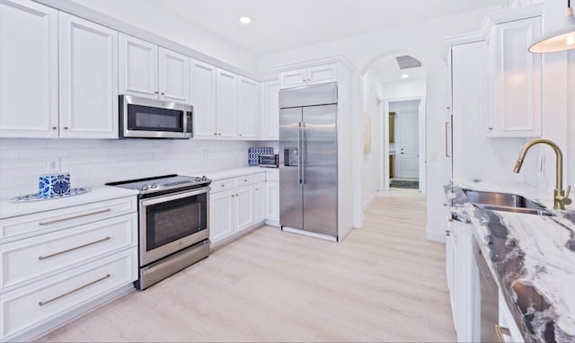 kitchen with light stone counters, tasteful backsplash, white cabinetry, appliances with stainless steel finishes, and sink