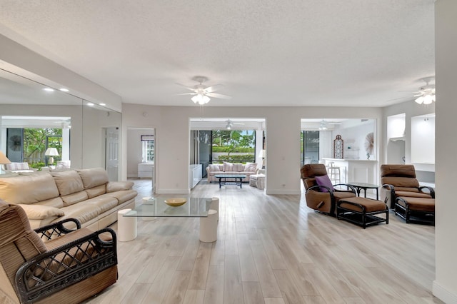 living area featuring light wood-style flooring, a textured ceiling, and baseboards