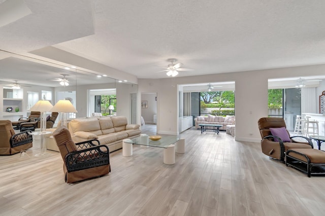 living area with a wealth of natural light, baseboards, a textured ceiling, and light wood-style floors