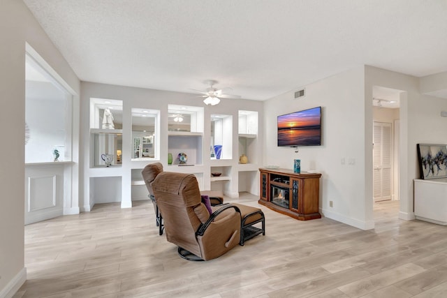 living area featuring a glass covered fireplace, light wood-style flooring, baseboards, and visible vents