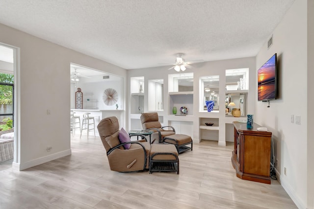 sitting room featuring light wood-type flooring, a ceiling fan, visible vents, and a textured ceiling