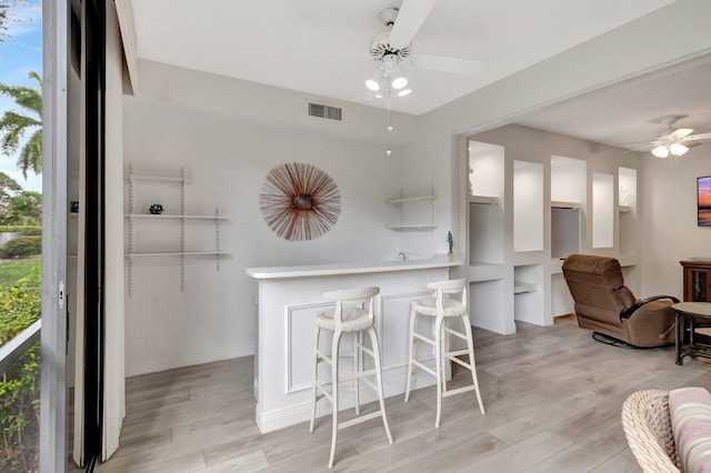 kitchen with visible vents, a kitchen bar, light wood-style floors, and a ceiling fan