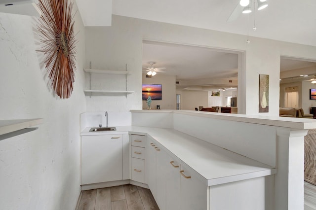 kitchen with a ceiling fan, light wood finished floors, a peninsula, a sink, and light countertops