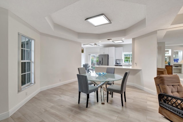 dining room featuring ceiling fan, baseboards, a tray ceiling, and light wood-style floors