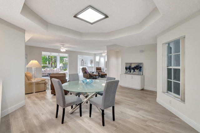 dining area featuring a tray ceiling, light wood-style flooring, and baseboards