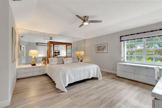 bedroom featuring ceiling fan, light wood-style floors, baseboards, and a textured ceiling