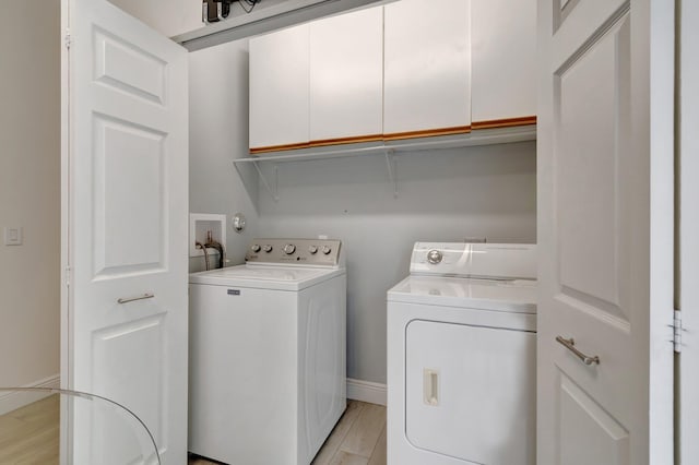 clothes washing area with washer and dryer, cabinet space, light wood-type flooring, and baseboards