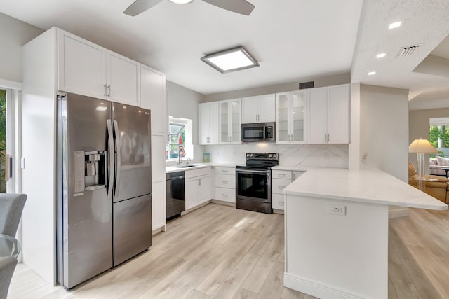 kitchen featuring visible vents, light wood finished floors, a peninsula, stainless steel appliances, and glass insert cabinets