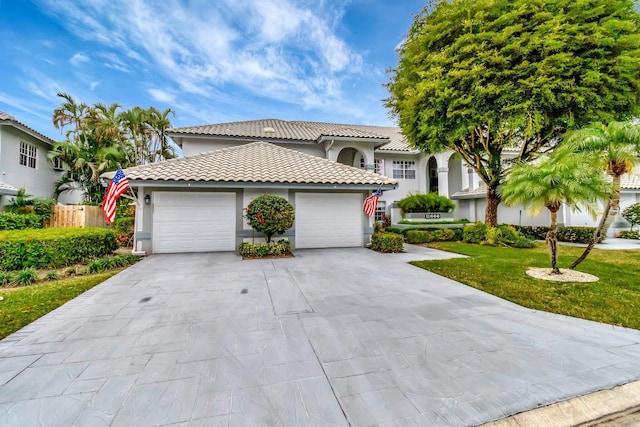 mediterranean / spanish home with a tiled roof, concrete driveway, a front yard, stucco siding, and an attached garage