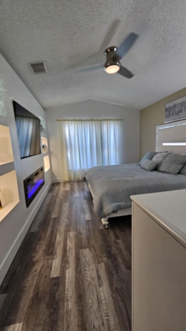 bedroom featuring ceiling fan, dark hardwood / wood-style floors, vaulted ceiling, and a textured ceiling