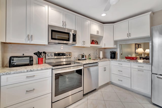 kitchen with appliances with stainless steel finishes, white cabinetry, sink, light stone counters, and light tile patterned floors