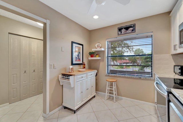 kitchen with light tile patterned floors, white cabinetry, stainless steel electric range oven, ceiling fan, and tasteful backsplash