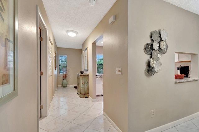 hall with a textured ceiling and light tile patterned flooring