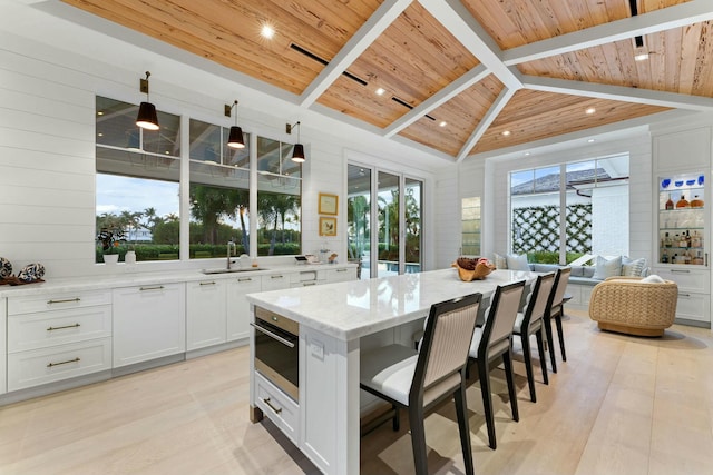 kitchen with sink, white cabinets, light stone counters, pendant lighting, and wood ceiling