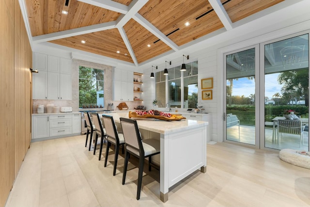 kitchen featuring light stone counters, wood ceiling, decorative backsplash, a kitchen island, and white cabinetry