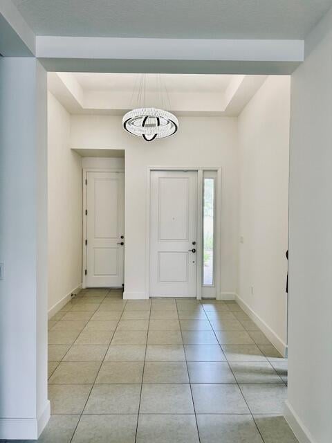 tiled entryway with a tray ceiling and a notable chandelier