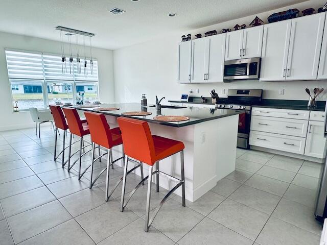 kitchen with a kitchen breakfast bar, white cabinets, stainless steel appliances, and an island with sink