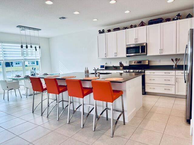 kitchen with a breakfast bar, hanging light fixtures, appliances with stainless steel finishes, an island with sink, and white cabinets