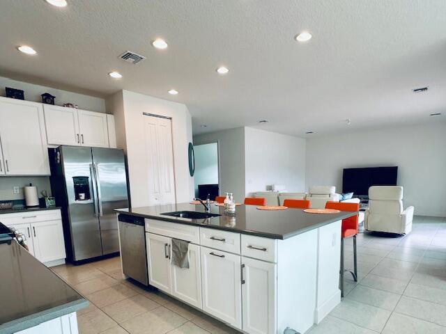 kitchen with light tile patterned floors, white cabinetry, an island with sink, appliances with stainless steel finishes, and sink