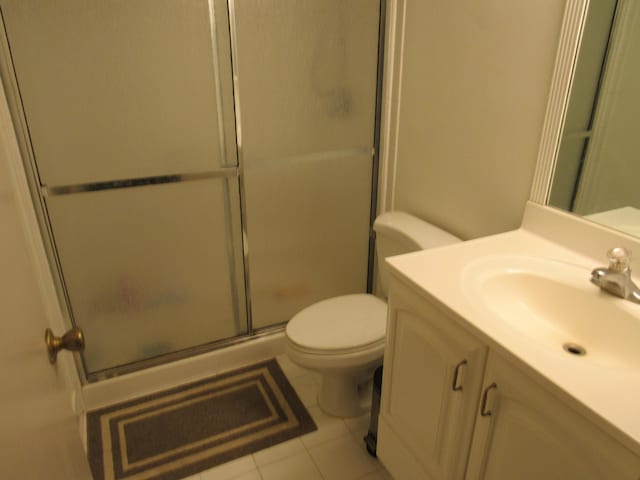 bathroom featuring toilet, vanity, tile patterned floors, and a shower with shower door