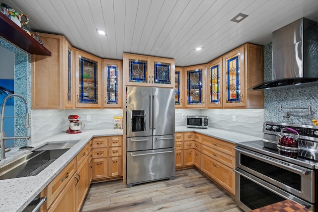 kitchen with light stone countertops, appliances with stainless steel finishes, wall chimney range hood, sink, and backsplash