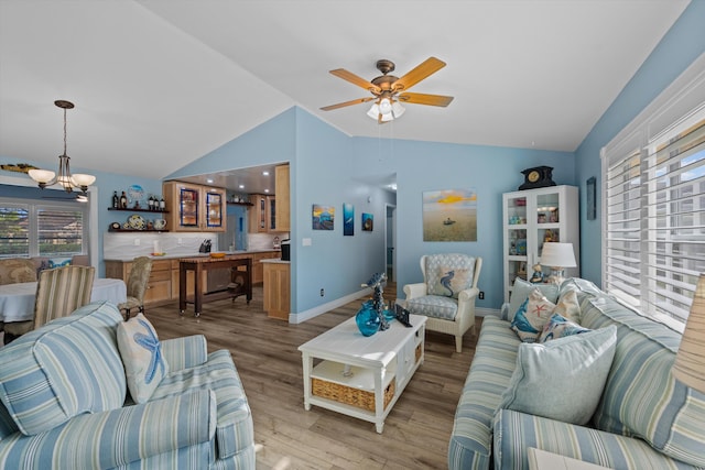 living room featuring vaulted ceiling, ceiling fan with notable chandelier, and light hardwood / wood-style flooring