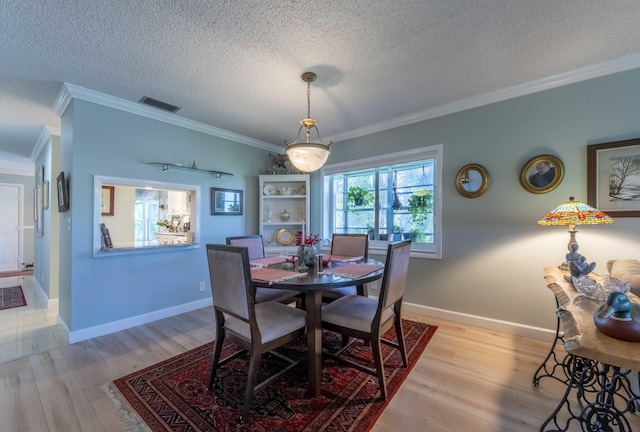 dining room with light wood-type flooring, ornamental molding, and a textured ceiling