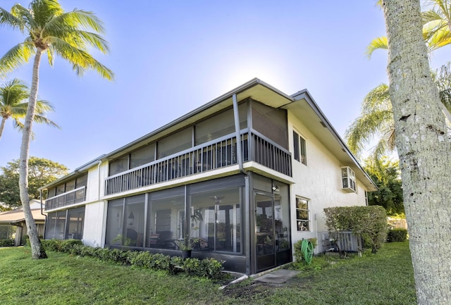 rear view of property with a wall unit AC, a sunroom, a lawn, and central air condition unit