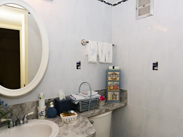 bathroom featuring tile walls, toilet, decorative backsplash, and sink