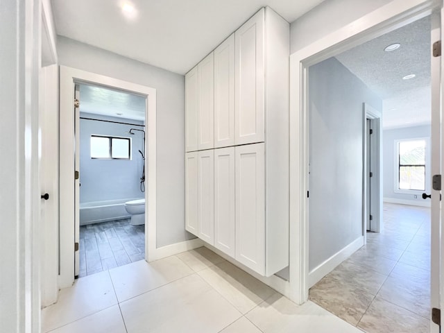 hallway featuring plenty of natural light, a textured ceiling, and light tile patterned flooring