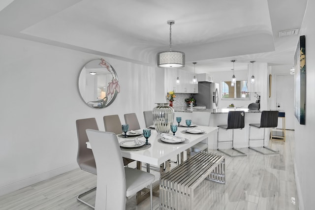 dining area featuring a raised ceiling and light hardwood / wood-style flooring