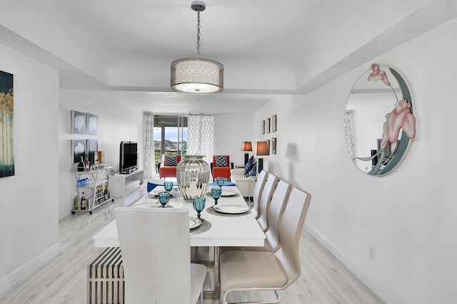 dining area with a tray ceiling and light hardwood / wood-style flooring