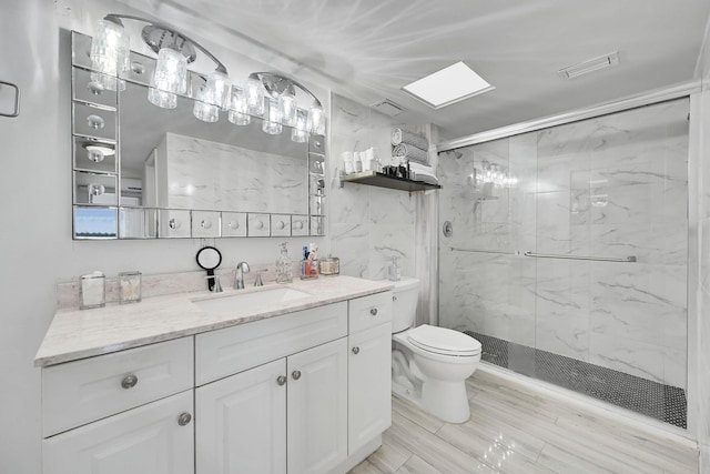 bathroom featuring toilet, a shower with door, a skylight, and vanity