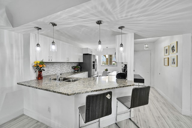 kitchen featuring kitchen peninsula, pendant lighting, stainless steel fridge, white cabinetry, and sink