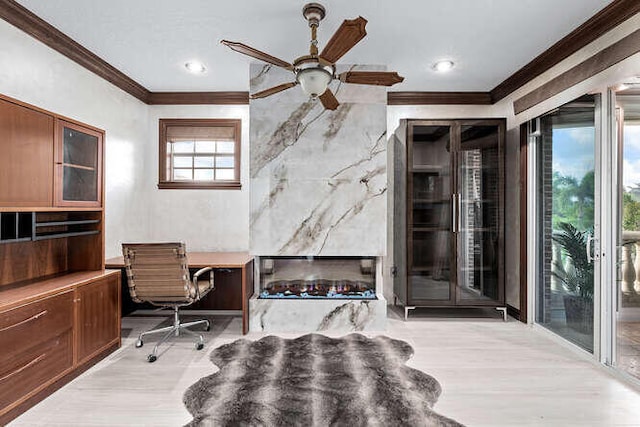 office space featuring a fireplace, ornamental molding, ceiling fan, and light wood-type flooring