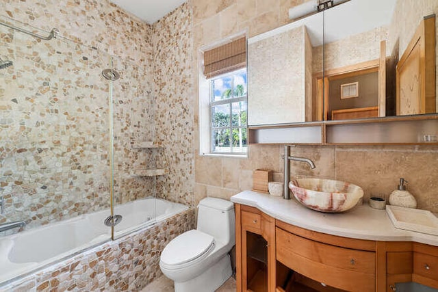 full bathroom featuring tiled shower / bath, tasteful backsplash, tile walls, vanity, and toilet