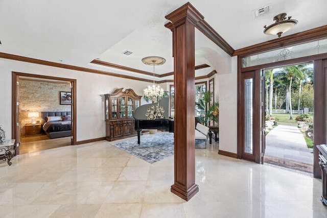 entrance foyer featuring a notable chandelier, ornamental molding, a tray ceiling, and ornate columns