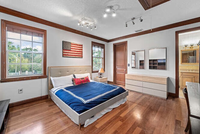 bedroom featuring crown molding, hardwood / wood-style flooring, track lighting, and a textured ceiling