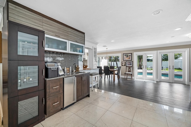 kitchen with sink, dark brown cabinetry, ornamental molding, decorative light fixtures, and french doors