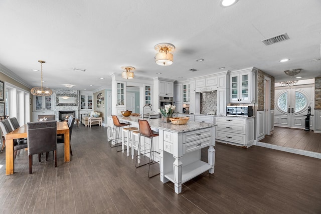 kitchen with white cabinetry, stainless steel appliances, light stone countertops, an island with sink, and decorative light fixtures