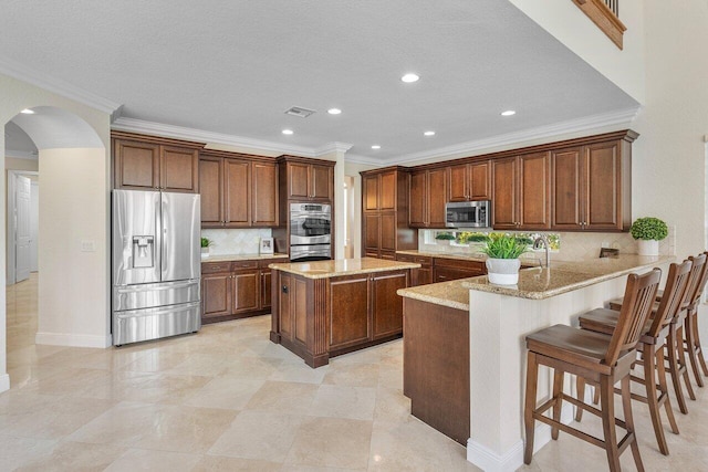 kitchen with stainless steel appliances, ornamental molding, kitchen peninsula, a kitchen island, and a breakfast bar