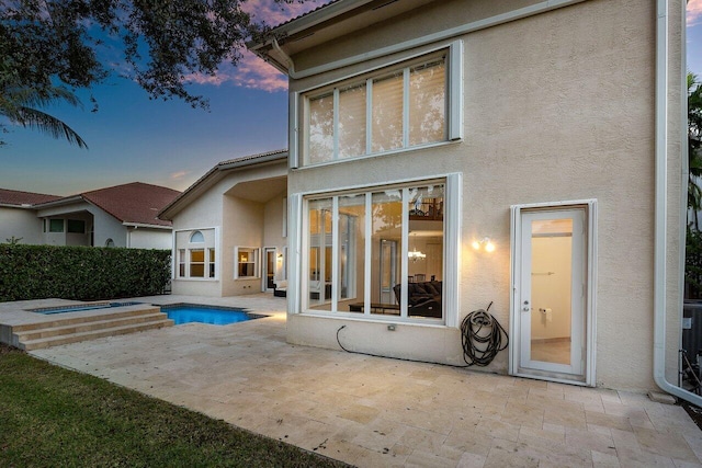 back house at dusk with a swimming pool with hot tub and a patio