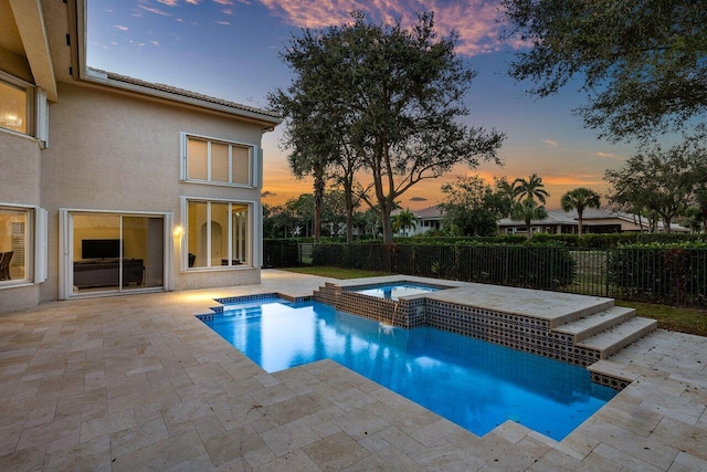 pool at dusk featuring a patio and an in ground hot tub