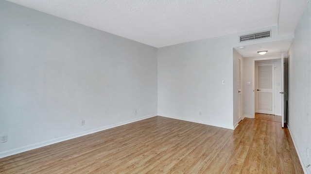 spare room featuring light wood-type flooring, baseboards, visible vents, and a textured ceiling