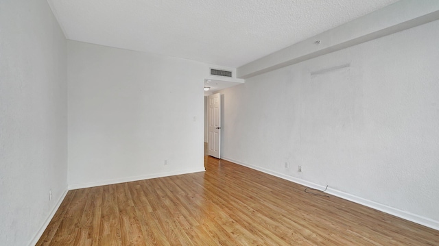 unfurnished room with light wood-style flooring, a textured ceiling, visible vents, and baseboards