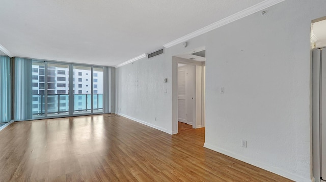 unfurnished room featuring expansive windows, ornamental molding, and light wood-type flooring