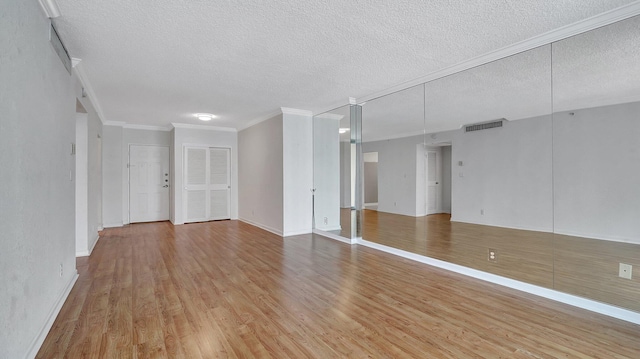 spare room featuring visible vents, ornamental molding, a textured ceiling, wood finished floors, and baseboards