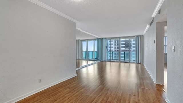 unfurnished room with a textured wall, wood finished floors, baseboards, ornamental molding, and a wall of windows