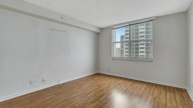 unfurnished room featuring a textured ceiling, baseboards, and wood finished floors