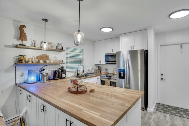 kitchen with stainless steel appliances, white cabinets, decorative light fixtures, sink, and butcher block counters